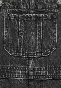 Svarta denim överdelar har en fyrkantig ficka med dubbelsöm, lätt textur och metallbeslag vid axlarna.