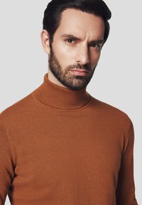 Brązowy sweter z golfem wykonany z dzianiny, charakteryzujący się dopasowanym krojem i prążkowanym kołnierzem, na neutralnym tle.