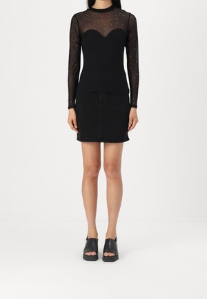 Woman wearing a sheer black long-sleeve top with small embellishments and a black mini skirt, paired with black open-toe platform sandals.