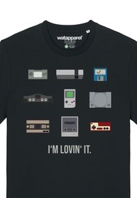 T-shirt noir avec des illustrations graphiques de diverses consoles de jeu en gris, vert, rouge et bleu. Le texte en dessous indique "JE L'AIME."