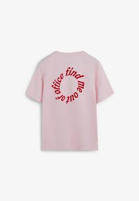 Camiseta de algodón rosa con mangas cortas. La parte trasera presenta un texto rojo en un diseño circular: "encuéntrame fuera de la oficina". Textura suave, estilo casual.