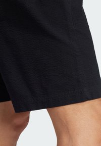 Black shorts made of textured fabric, featuring a straight hem and a subtle pattern, offering a relaxed fit at the thigh.