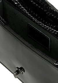 Vnitřek černé kožené kabelky s zipovou kapsou, řetízkovým detailem a hladkým povrchem. Obsahuje kovovou sponu na zavírání.