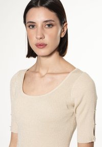 Top in maglia a coste color avorio con scollo rotondo, maniche corte e aperture decorative sui polsini, caratterizzato da un leggero luccichio.