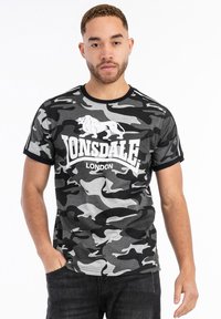 Szürke kamuflázs pamut póló, fehér "Lonsdale London" logóval és oroszlán grafikával, fekete kerek nyakkal és ujjakkal.