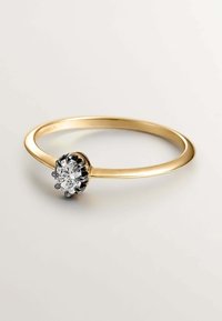 Anillo de oro con un diamante redondo central engastado en un prendedor de metal negro. La banda es lisa y delgada con un acabado pulido.