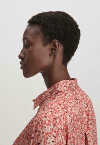 Camicia a fantasia rossa e rosa con colletto, caratterizzata da una vestibilità ampia e una texture di tessuto morbido.