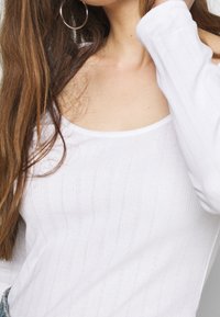 Witte longsleeve top met ribbelstructuur en een ronde halslijn, met een open schouderontwerp. Minimalistisch en naadloos uiterlijk.