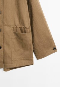 Bruine jas van gestructureerde stof, met een grote voorkantzak, knoopsluiting en een iets relaxte pasvorm.