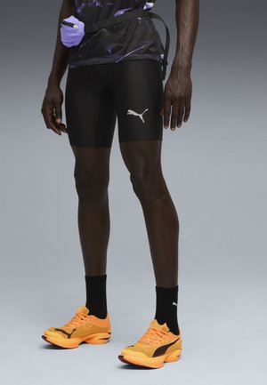 Black athletic shorts with a white Puma logo, paired with vibrant orange running shoes and black socks. Textured, form-fitting design.