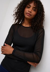 Haut noir à manches longues avec un design ajusté. Tissu transparent sur les manches, texture lisse, col rond et une subtile accentuation à la taille.