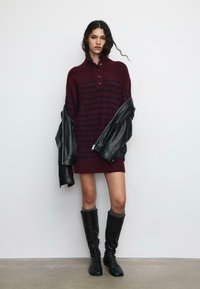 Haljina s prugama tamnocrvene boje s ovratnikom, uparena s crnom kožnom jaknom, crnim čizmama do koljena i sivim čarapama. Glatka tekstura, ležerni dizajn.