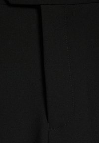 Detaliu al unei perechi de pantaloni din țesătură neagră, evidențiind un pliu vertical și cusături vizibile, creând un aspect neted și structurat.