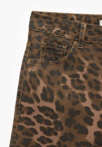 Pantaloni in denim con stampa leopardata, caratterizzati da uno sfondo marrone e macchie nere, design a cinque tasche e dettagli di cucitura in vista.