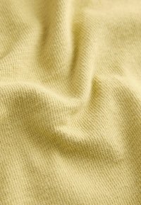 Texturált, lágy sárga színű szövet, finom kötött mintával, lágy hullámzással és sima, könnyű megjelenéssel.