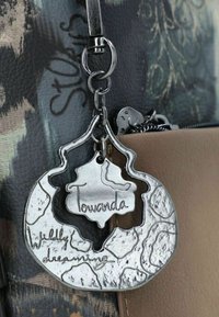 Porte-clés en métal avec une finition argentée texturée, portant les inscriptions "Towanda" et "Rêvant follement", fixé à un sac.