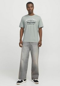 Lysegrøn bomulds T-shirt med "JACK & JONES Surfer's Club" trykt i marineblå og hvid. Sammen med løstsiddende lysegrå jeans og sorte sneakers.