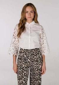 Witte blouse met geborduurde kantmouwen, gecombineerd met beige en zwart luipaardprint brede broekspijpen. Glad materiaal met ingewikkelde details.