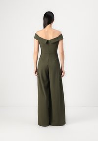 Jumpsuit verde oliva senza spalline con design a gamba larga, dotato di una cerniera posteriore e un busto strutturato. Tessuto dalla texture liscia.