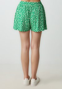 Shorts floreali verdi con una cintura elastica arricciata, dalla vestibilità ampia e tessuto leggero, che arrivano sopra il ginocchio. Motivi floreali bianchi su tutto il capo.
