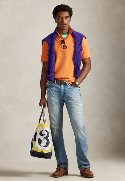 Πορτοκαλί πόλο πουκαμίσα, μοβ πουπουλένο γιλέκο, μπλε τζιν με σκισίματα, καφετιά μοκασίνια και μια τσάντα ώμου σε κίτρινο, μπλε και λευκό με γραφικό σχέδιο.