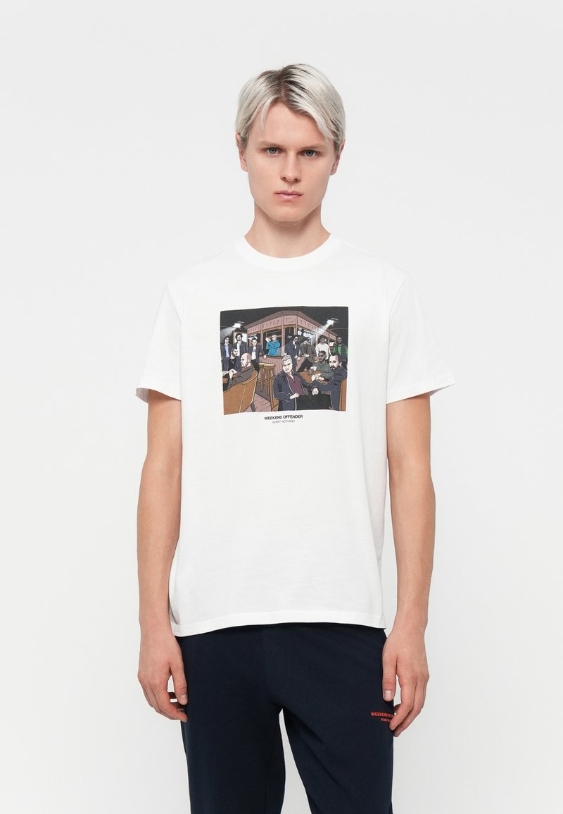 White cotton t-shirt featuring a colorful graphic print of people in a bar scene, with a round neckline and short sleeves.
