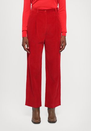 Person wearing high-waist red corduroy wide-leg pants, matching red long-sleeve top, and brown ankle boots standing against plain background.