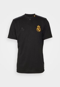 Černý síťový dres s límcem na knoflíky, zdobený zlatým logem klubu a černým brandingem Adidas. Šedé akcentní pruhy na ramenech.