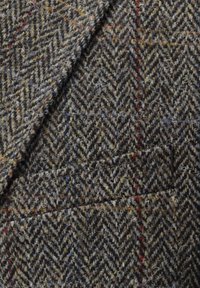 Tweed-Stoff mit Fischgrätmuster in erdigen Tönen, mit subtilen roten und gelben Sprenkeln. Strukturierte Oberfläche mit weichem Finish.