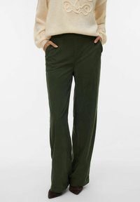 Zielone szerokie spodnie o gładkiej fakturze, z bocznymi kieszeniami i elastycznym paskiem, zestawione z kremowym swetrem.