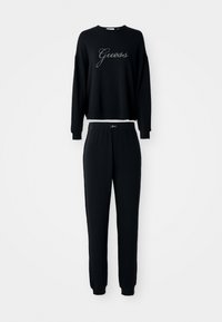 Schwarzes Langarm-Sweatshirt und passendes Jogginghosen-Set, beide mit "Guess"-Logo in Schriftzug auf der Brust und dem Bund.