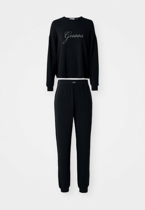 Crni dukserica dugih rukava i odgovarajući set donjih hlača s jogger krojem, oboje s "Guess" logom u pisanom fontu na prsima i po pojasu.