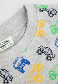 Szara bawełniana koszulka z kolorowymi wzorami monster trucków (niebieski, zielony, żółty) z przodu, z okrągłym dekoltem i widoczną metką.