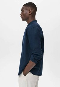 Navy long-sleeve shirt in a relaxed fit with a rounded collar and rolled cuffs, made from lightweight fabric, paired with light-colored trousers.