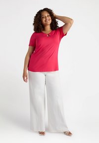 T-shirt rosso a maniche corte con dettaglio a chiave sul collo, abbinato a pantaloni bianchi a gamba larga e sandali leggeri. Texture liscia.