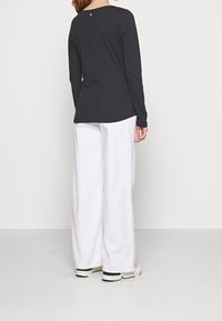 Maglietta a maniche lunghe grigia scura con scollatura tonda, abbinata a pantaloni bianchi a gamba larga, indossata con sneakers chiare. Dettaglio posteriore notevole visibile.