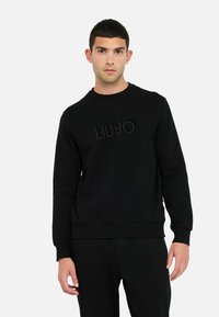 Černá mikina vyrobená z měkké látky, na přední straně s texturovaným logem "LIUJO", kulatý výstřih a žebrované manžety a lem.