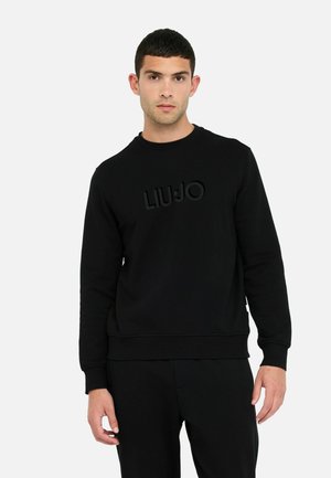 Melnā sporta krekls, kas izgatavots no mīksta auduma, ar strukturētu logo "LIUJO" priekšā, apaļu kaklu un ribotām piedurknēm un apakšmalu.