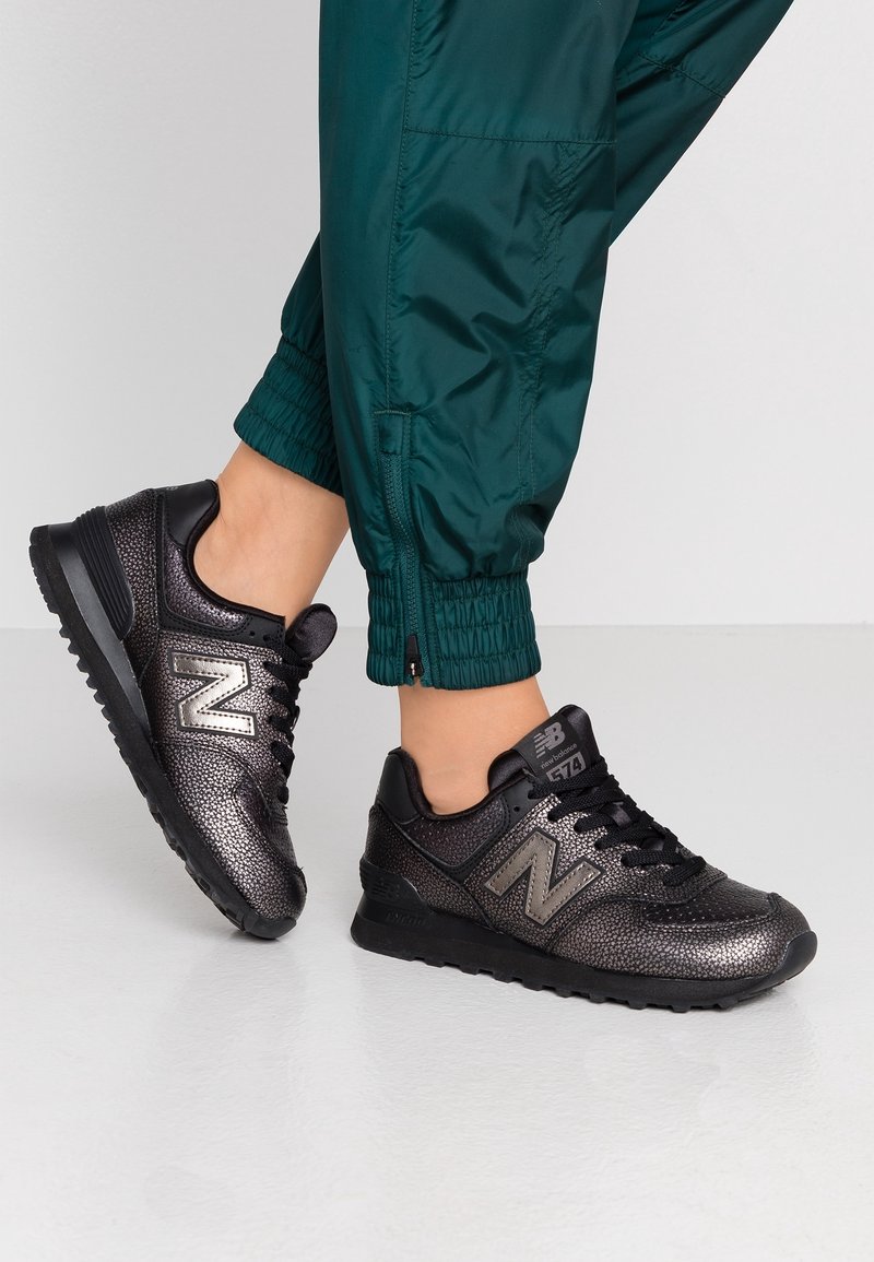 Schwarze Sneaker mit einer strukturierten, metallischen Oberfläche und reflektierenden Akzenten. Sie verfügen über ein Schnürdesign und das charakteristische 'N'-Logo an der Seite.