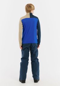 Top a maniche lunghe con design color block in blu, beige e blu scuro; abbinato a pantaloni blu scuro. Texture liscia, vestibilità atletica.