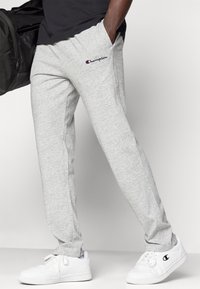 Graue Fleece-Jogginghosen mit Seitentaschen, gerippten Bündchen, gesticktem "Champion"-Logo und lockerer Passform. Kombiniert mit weißen Sneakern.