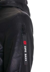 Zwart lederen jack met een capuchon, voorzien van een zijzak met een zwart en rode label met de tekst "CIPO BAXX" en een gestructureerd oppervlak.