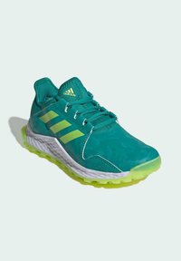 Baskets de sport teal avec des accents vert lime, tige texturée, semelle blanche et semelle multidirectionnelle pour l'adhérence. Présente un logo avec trois bandes.