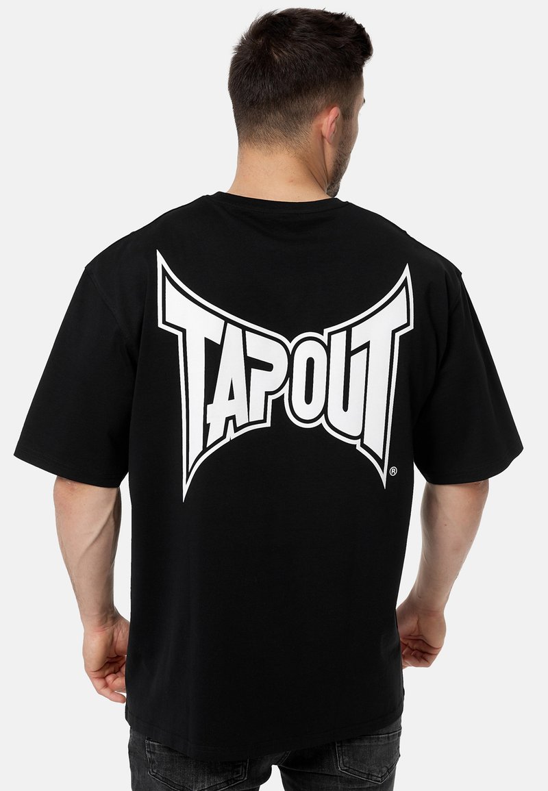 Fekete pamut póló, nagy fehér "TAPOUT" logóval a háton. Rövid ujjú, laza fazonú, sima textúrájú anyag.