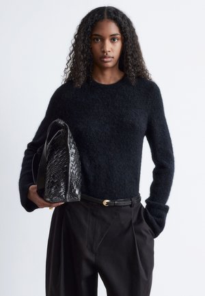 Schwarzer Strickpullover mit langen Ärmeln, kombiniert mit schwarzen hoch taillierten Hosen und einer strukturierten, gewebten schwarzen Handtasche.