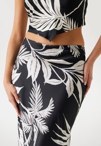 Set din țesătură neagră, format dintr-un top scurt și o fustă lungă, ornate cu mari modele de frunze albe. Textură netedă, cu o siluetă ajustată.