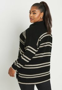 Pull en tricot rayé noir et beige avec un col montant, des manches longues et des fentes sur les côtés. Tissu texturé avec une coupe ample.