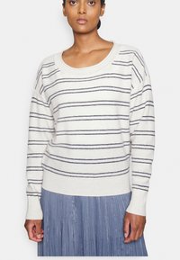 Krämfärgad tröja med marinblå vågräta ränder, ribbad halsringning och manschetter. Modellen har på sig en veckad ljusblå kjol för kontrast.