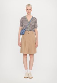 Striped short-sleeve cardigan with green buttons, beige pleated shorts, and a small blue crossbody bag. Beige shoes with light-colored soles.