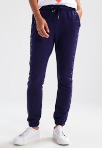 Navy blue sweatpants with elastic cuffs, featuring silver studded detailing along the sides and a drawstring waist for adjustable fit.